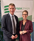 Auf dem Bild sieht man links einen Mann in grauem Anzug und rechts eine Frau im weinroten Hosenanzug vor dem Roll-Up mit dem grünen Logo der Europa-Union Deutschland.